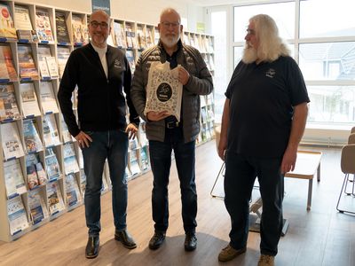 Buesum-Gaestelotsen-25000-Teilnehmer2.jpg (v. l. n. r.): TMS Büsum Geschäftsführer Oliver Münch, Ehrengast Roland Werner und Gästelotse Raimund Donalies bei der Gästebegrüßung mit Ehrung im Watt’n Hus Büsum.