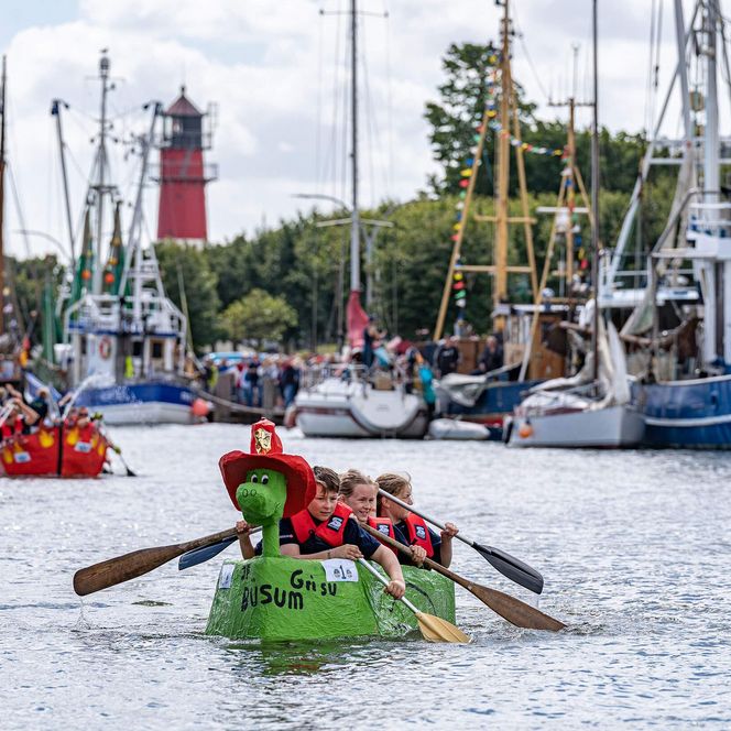 An den Büsumer Kutterregattatagen paddeln Kinder während der Papierbootregatta mit ihren selbstgebauten Booten durch den Hafen.