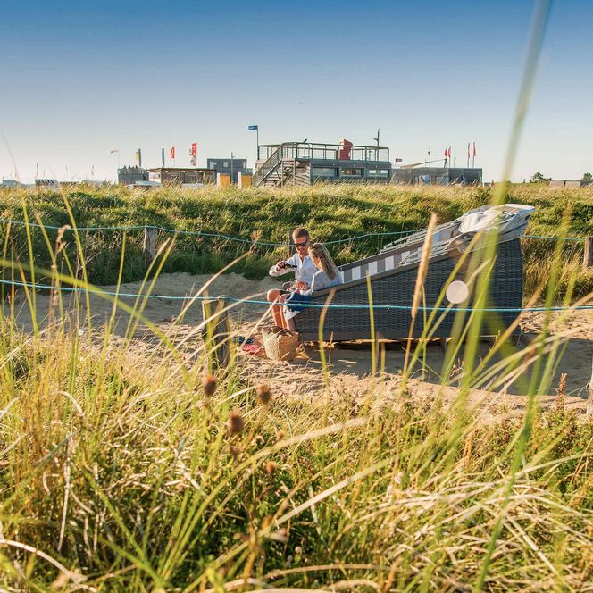 Ein Paar sitzt im Büsumer Schlafstrandkorb zwischen den Dünen auf der Watt'n Insel.