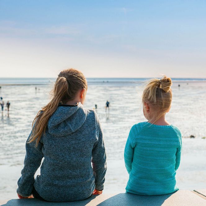 Zwei kleine Mädchen sitzen auf der Watt'n Insel in Büsum und blicken aufs Wattenmeer.