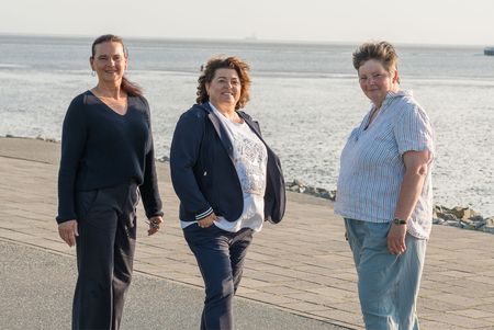 Drei Personen stehen am Strand, im Hintergrund ist das Wattenmeer zu sehen