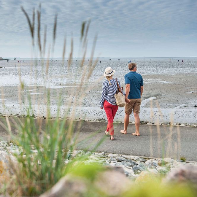 Ein Paar geht spazieren am Büsumer Deich und blickt aufs Wattenmeer.