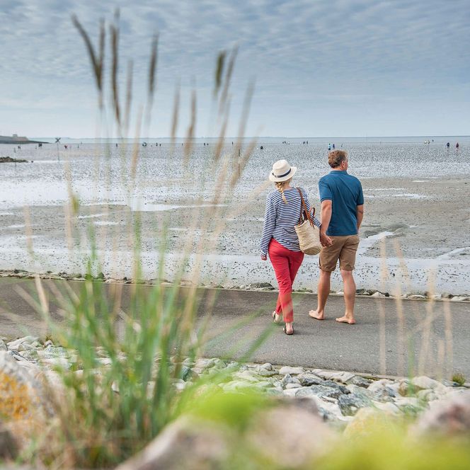 Ein Paar geht spazieren am Büsumer Deich und blickt aufs Wattenmeer.