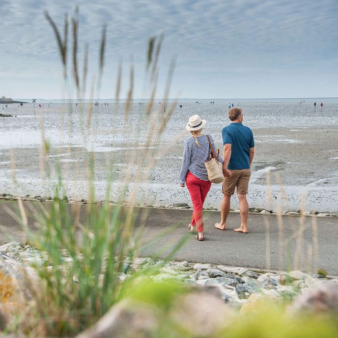 Ein Paar geht spazieren am Büsumer Deich und blickt aufs Wattenmeer.