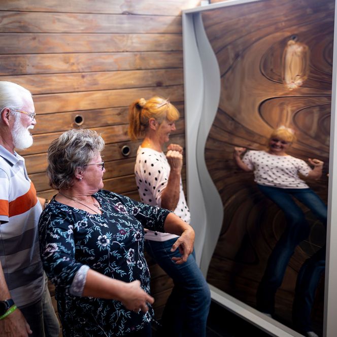 Drei Erwachsene bewegen sich vor einem wellenförmigen Spiegel im Erlebniszentrum und Mitmachmuseum Phänomania Büsum.
