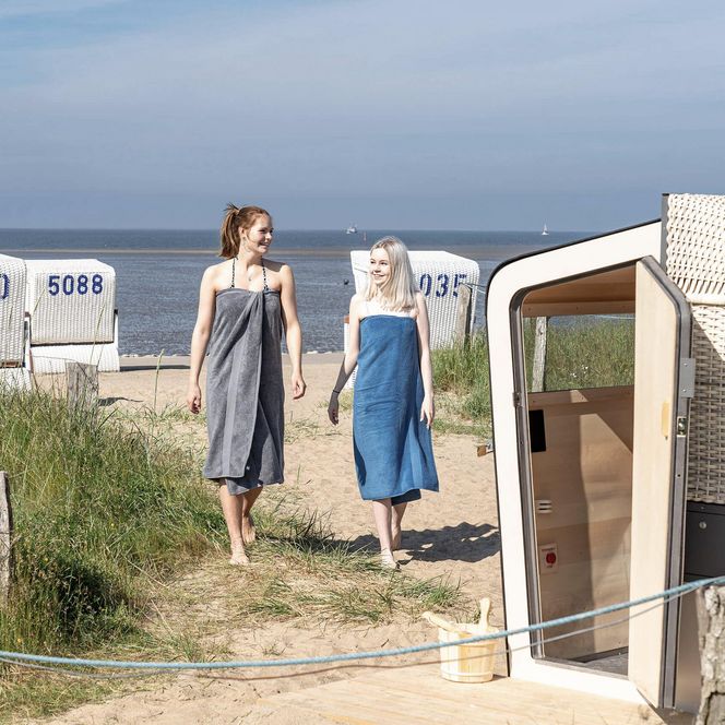 Zwei Frauen laufen über den Strand zur Strandkorbsauna auf der Familienlagune in Büsum.
