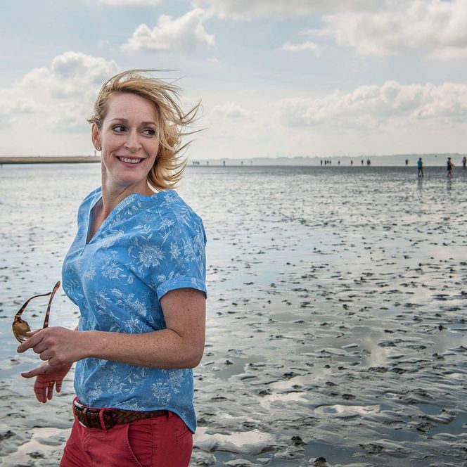 Eine fröhliche Frau steht im Watt vor Büsum.