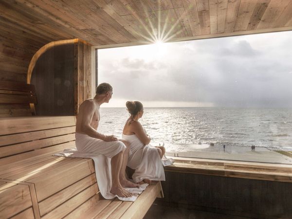Ein Paar schaut aus dem Panoramafenster der Sauna in der Meerzeit Büsum aufs Meer.