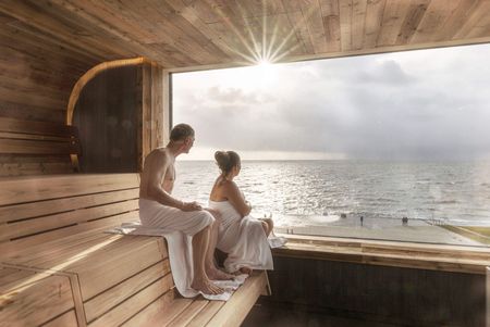 Ein Paar schaut aus dem Panoramafenster der Sauna in der Meerzeit Büsum aufs Meer.
