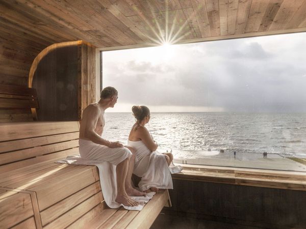 Ein Paar schaut aus dem Panoramafenster der Sauna in der Meerzeit Büsum aufs Meer.