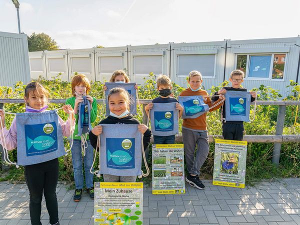 Kinder stehen mit Schildern vor einer Blumenwiese.