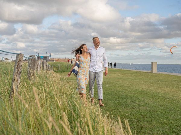 Ein junges Paar geht auf der Watt'n Insel in Büsum im Gras spazieren.