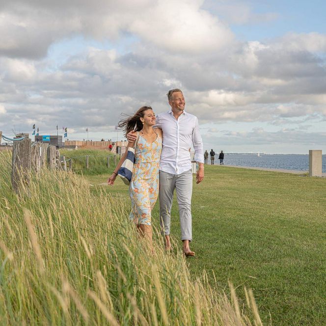 Ein junges Paar geht auf der Watt'n Insel in Büsum im Gras spazieren.