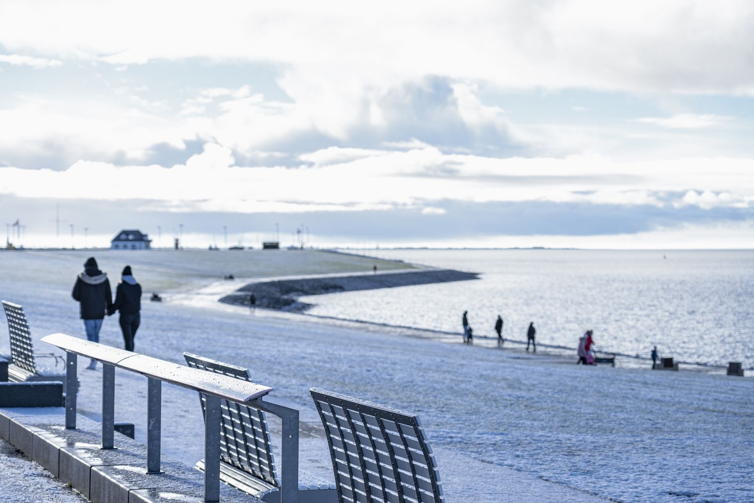 Deich mit Schnee mit Spaziergängern.