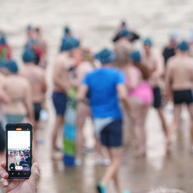Eine Person filmt die Menschen die zum Neujahrsanbaden in Büsum in die Nordsee gehen.
