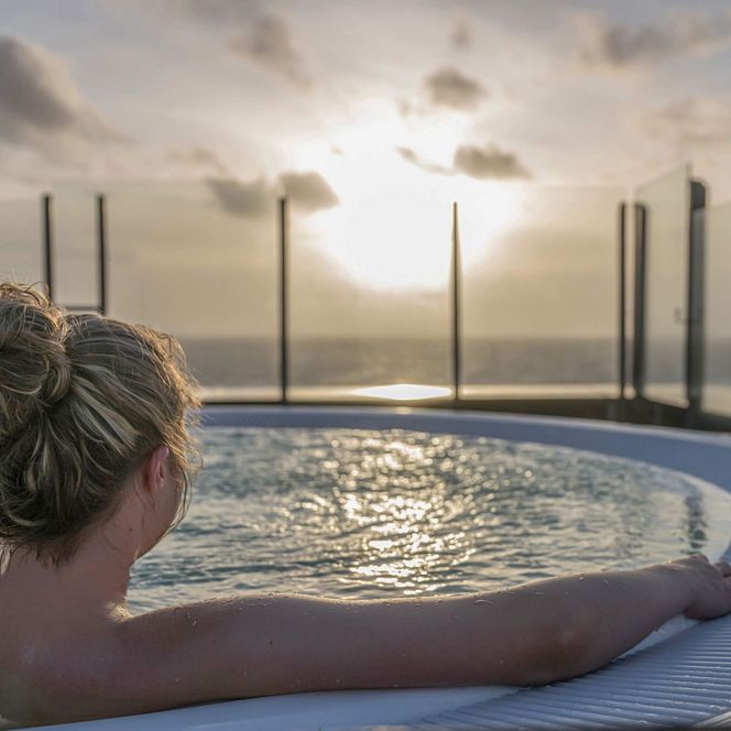Eine junge Frau sitzt im Whirlpool auf der Dachterrasse der Meerzeit Büsum und beobachtet den Sonnenuntergang.