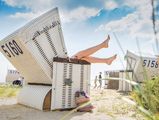 Eine Frau streckt ihre Beine aus einem Strandkorb am Sandstrand in Büsum.