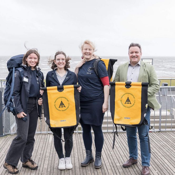Die Schutzstation Wattenmeer Vier Personen am Deisch mit zwei gelben Rucksäcken.