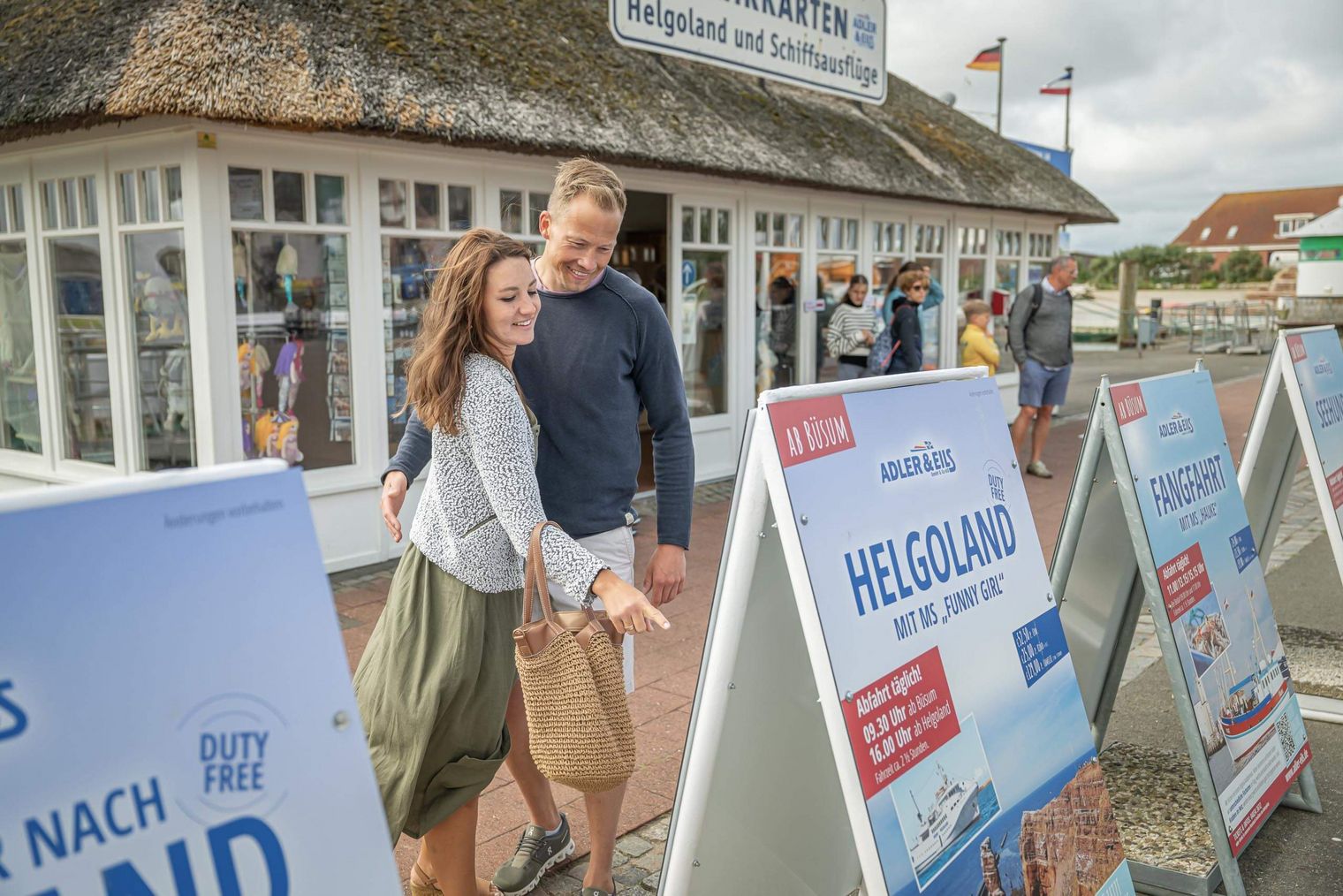 Ein junges Paar betrachtet die Schilder der Ausflugs-Schiffahrten am Büsumer Ankerplatz.