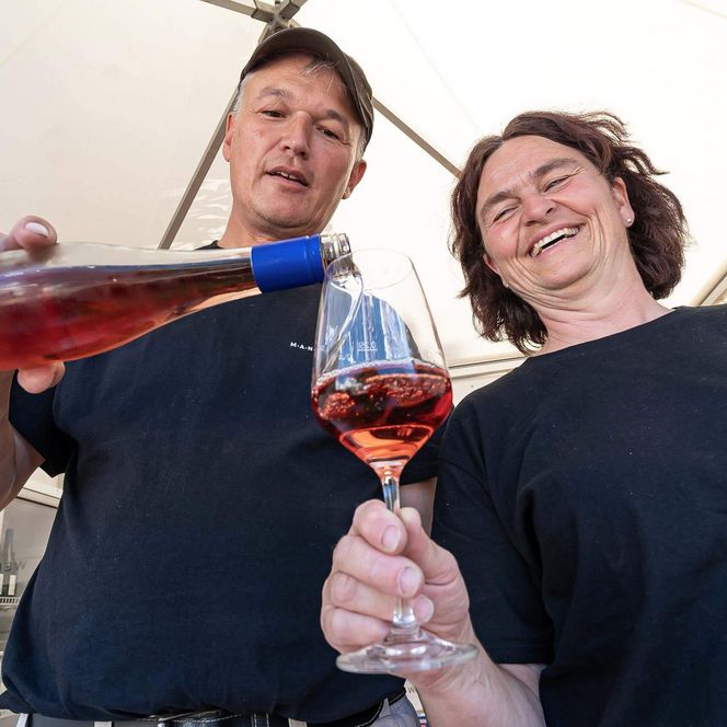 Ein Winzer aus Weinstadt gießt Wein in das Glas einer Frau auf dem Büsumer Winzerfest am Ankerplatz.