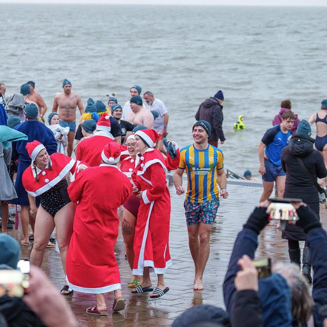 Viele Personen in Badekleidung und Verkleidungen nehmen beim Neujahrsanbaden in Büsum teil und werden von den Zuschauenden gefilmt.