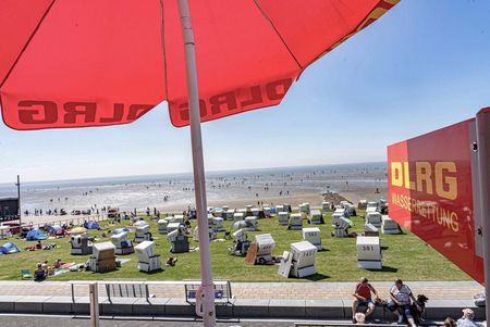 Ein roter Schirm und ein Schild mit DLRG Schriftzug mit Blick auf die Nordsee.