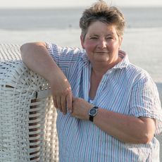 Eine Frau steht neben einem Strandkorb. Im Hintergrund ist das Wattenmeer.