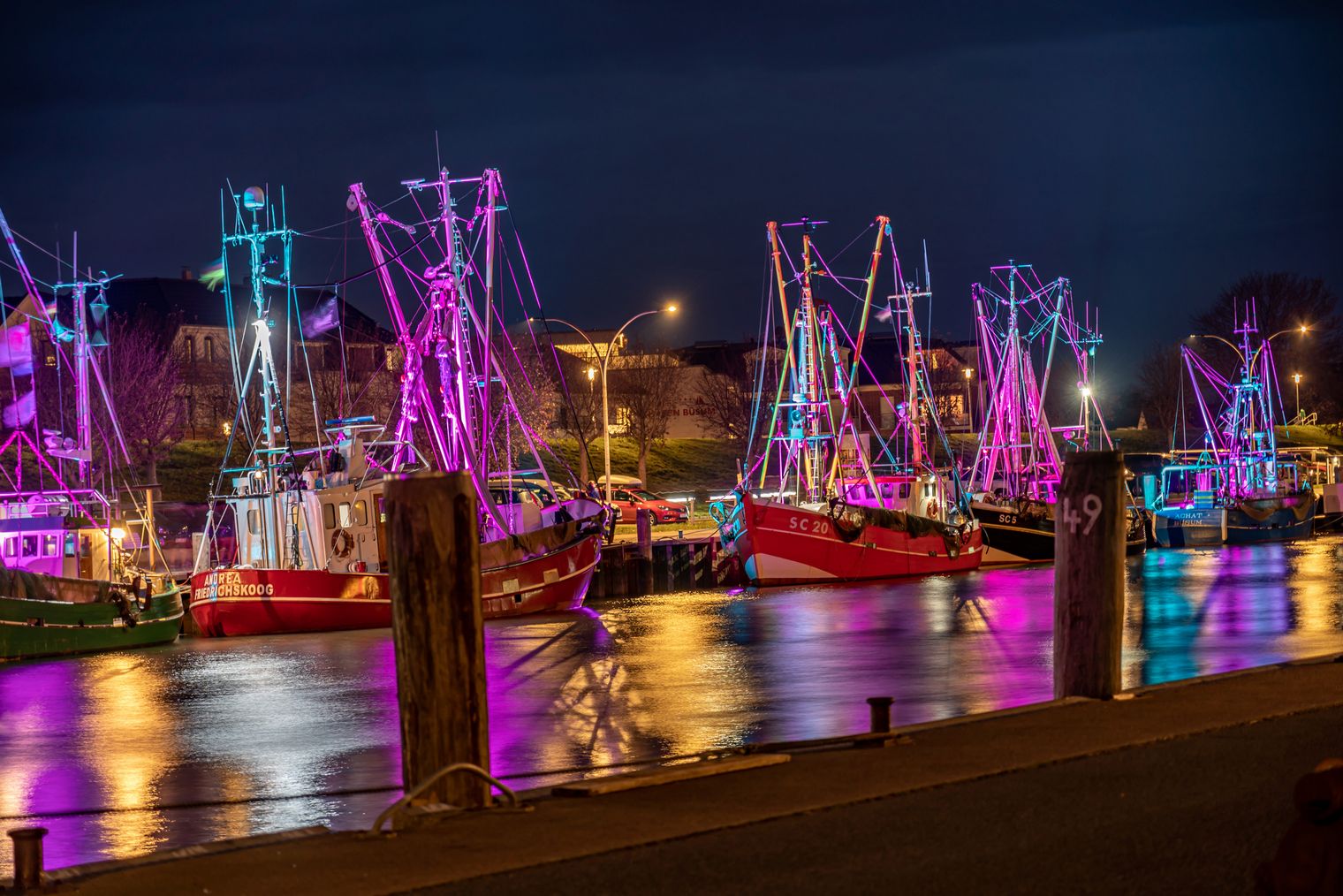 Kutter liegen bei Nacht im Hafen und werden mit bunten Lichtern erleuchtet.
