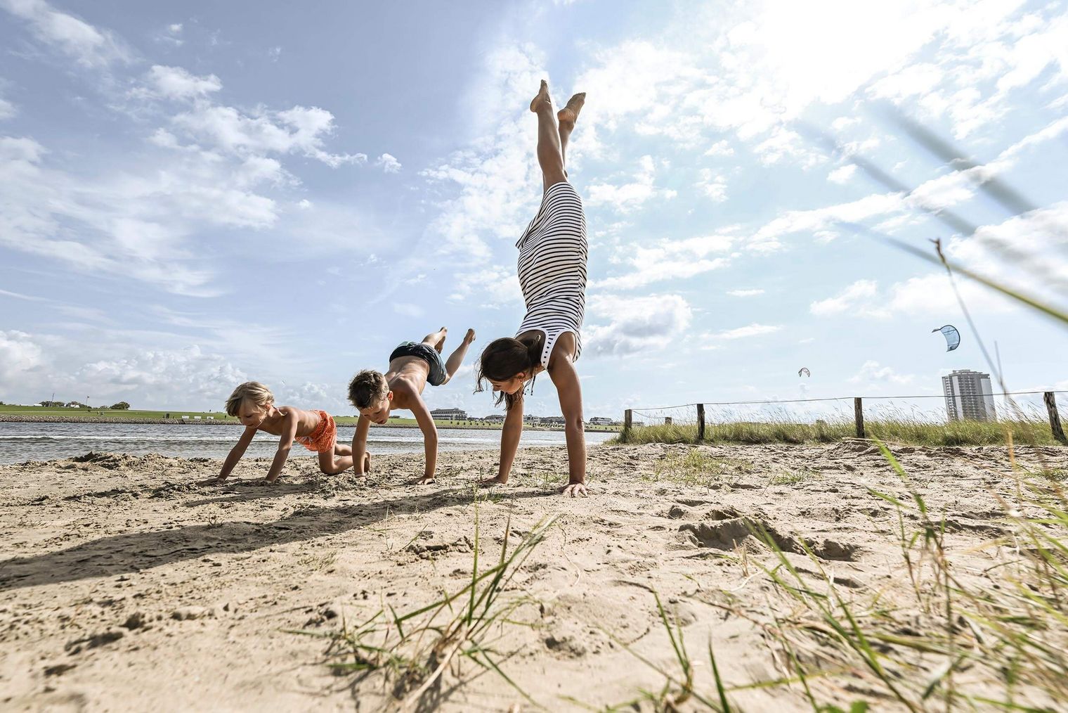 Eine junge Frau macht Handstand mit ihren Kindern am Sandstrand in Büsum.