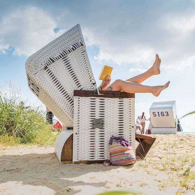 Eine Frau streckt ihre Beine aus einem Strandkorb am Sandstrand in Büsum.