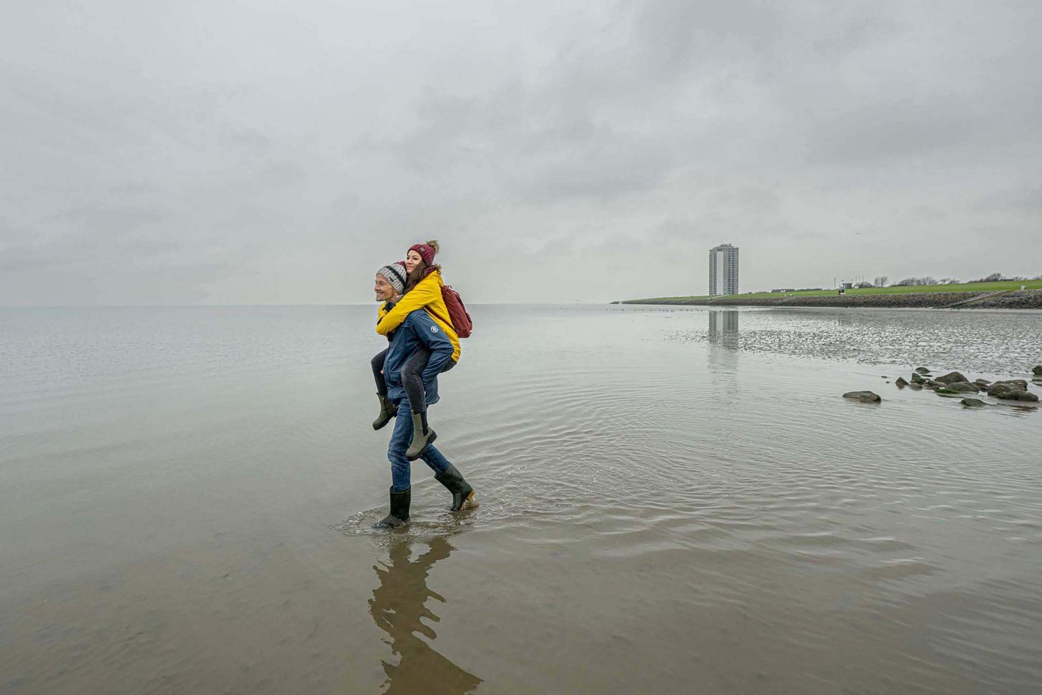 Ein Mann trägt seine Frau huckepack durch das Büsumer Wattenmeer.