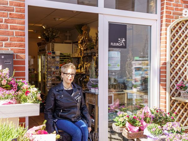 Eine Rollstuhlfahrerin rollt aus einem Büsumer Blumenladen.