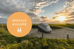 Der Schlafstrandkorb der Aktion Mensch bei Sonnenuntergang auf der Watt'n Insel in der Familienlagune. Daneben abgebildet das Logo der Sozialen Allianz.