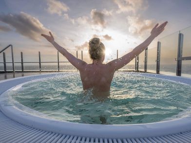 Eine junge Frau sitzt im Whirlpool auf der Dachterrasse der Meerzeit Büsum und beobachtet den Sonnenuntergang.
