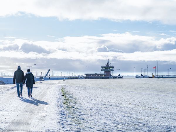 Spaziergänger auf dem verschneiten Deich laufen Richtung Schleuse.