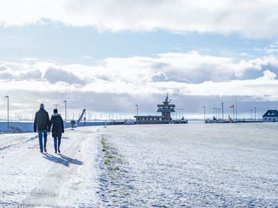 Spaziergänger auf dem verschneiten Deich laufen Richtung Schleuse.