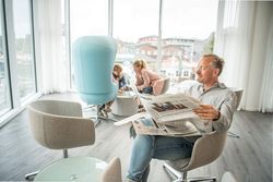 Ein Mann sitzt im Sessel und liest Zeitung im Wintergarten des Büsumer Watt'n Hus.