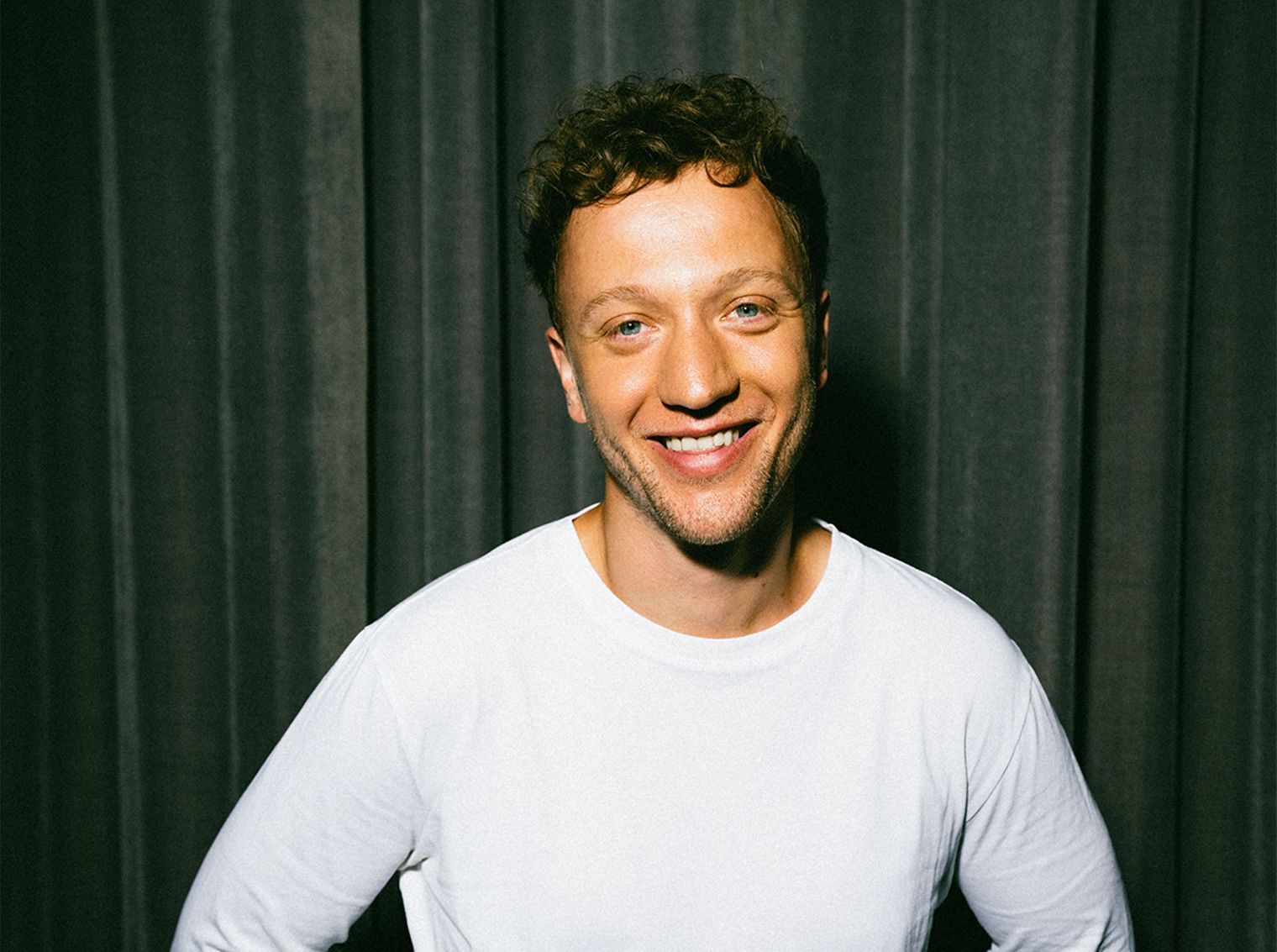 Ein junger Mann in weißem Langarmshirt lächelt in die Kamera.