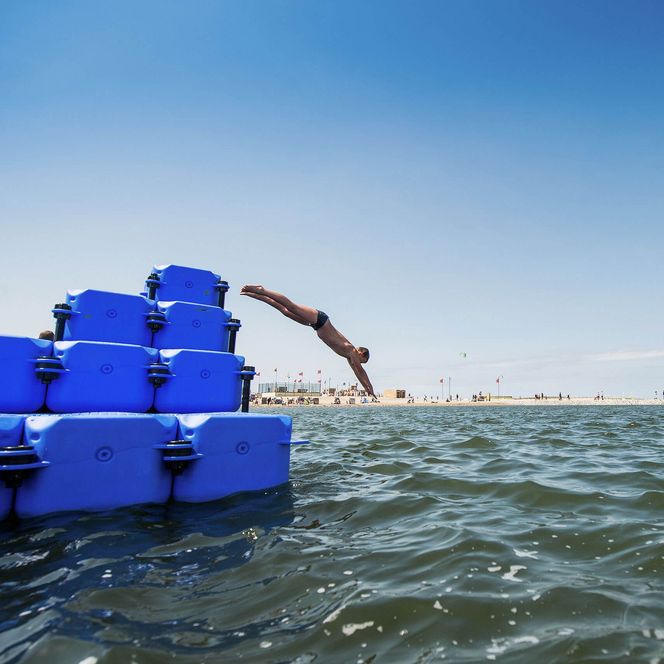 Ein Junge springt vom Schwimmponton in der Familienlagune Perlebucht in Büsum kopfüber ins Wasser.