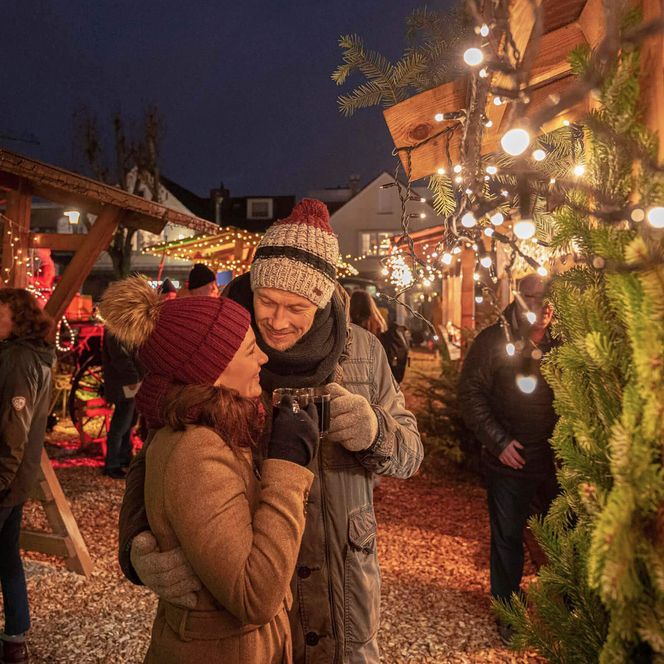 Ein Paar trinkt ein heißes Getränk vor einem Stand auf dem Weihnachtsmarkt in Büsum.
