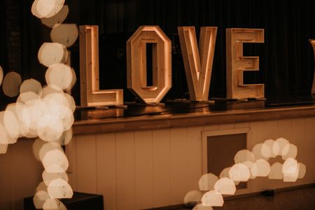 Das Wort "LOVE" in großen hölzernen Buchstaben, das von innen beleuchtet ist, steht auf einer Bühne.
