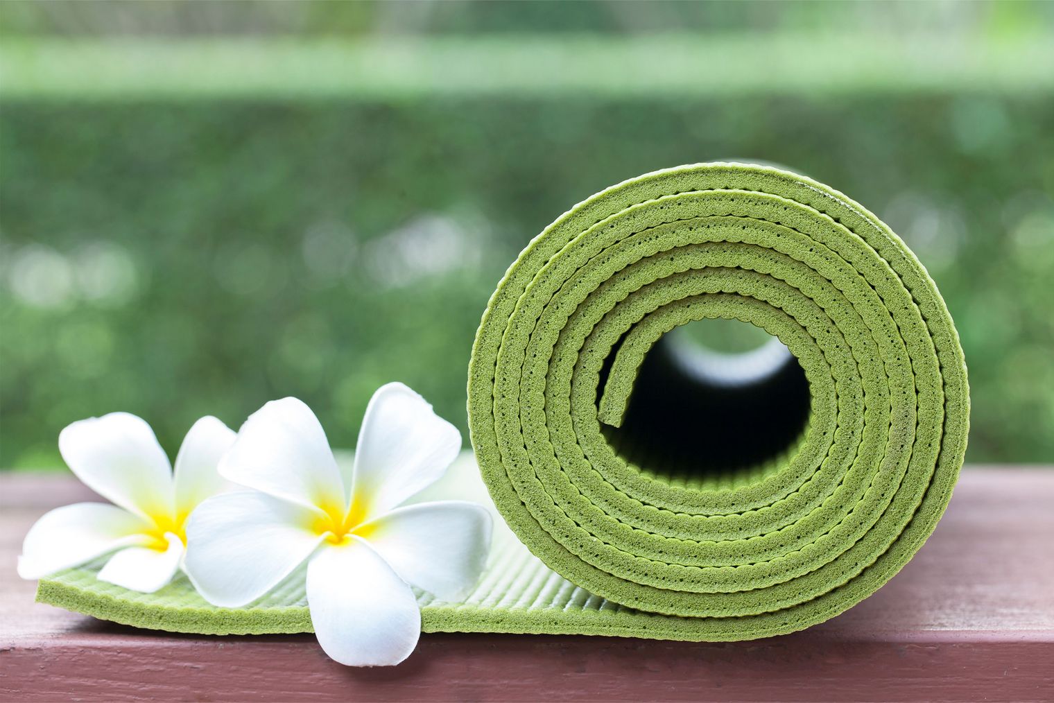 Eine grüne Yogamatte, die etwas aufgerollt ist. Darauf liegen zwei weiße Blüten.