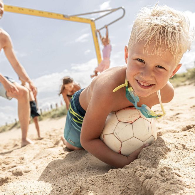 Ein Junge wirft sich auf seinen Ball am Sandstrand in Büsum.